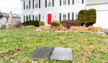 Damaged roof shingles laying on ground in front of home