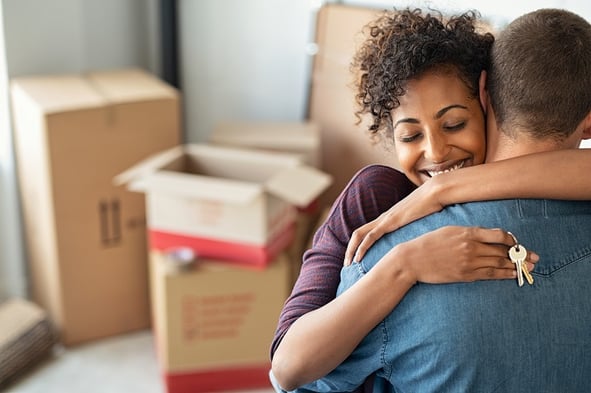 woman hugging man with moving boxes in background